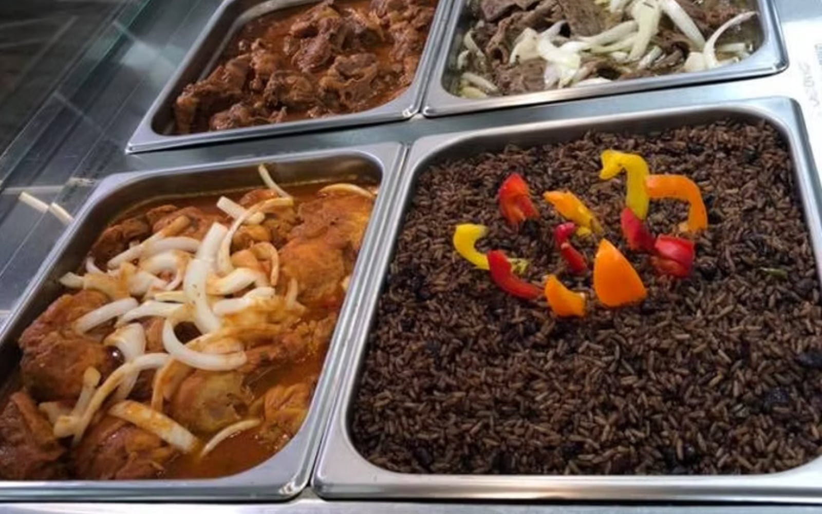Hot food bar at Latin Fresh Market Riverview showing braised meats, chicken with peppers, and seasoned potatoes in steel warming trays